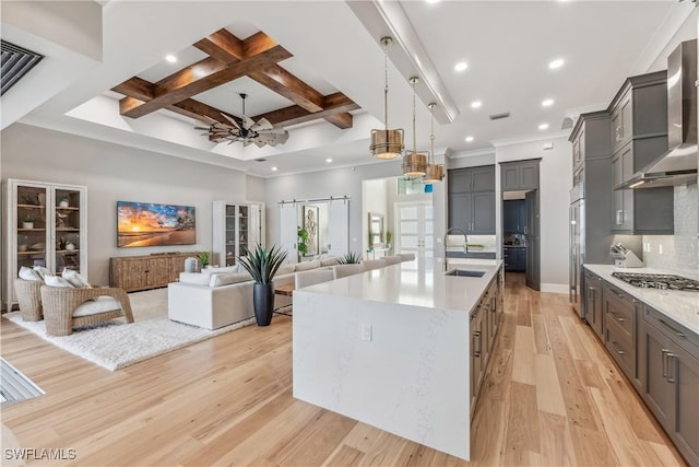 kitchen featuring pendant lighting, sink, coffered ceiling, a large island, and wall chimney range hood