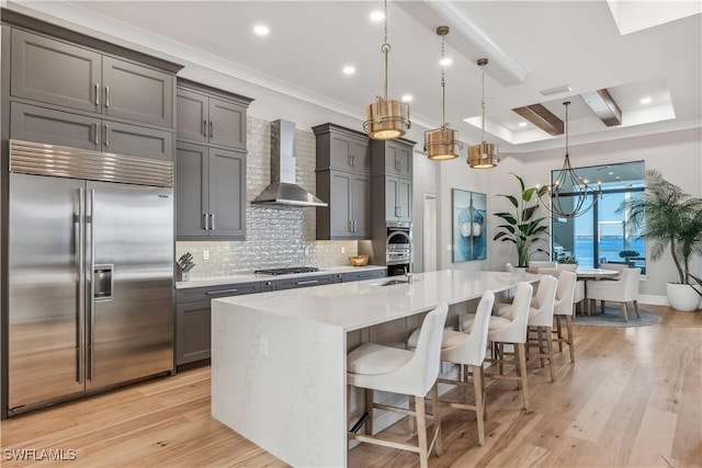 kitchen featuring pendant lighting, a breakfast bar area, a large island with sink, stainless steel appliances, and wall chimney range hood