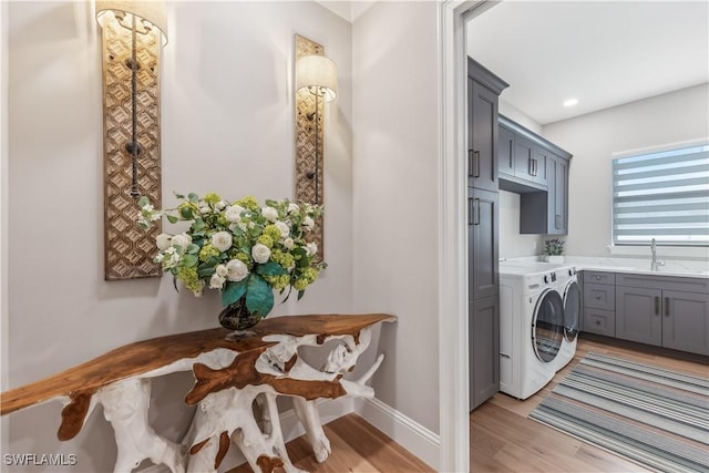 clothes washing area with cabinets, washing machine and dryer, sink, and light hardwood / wood-style flooring