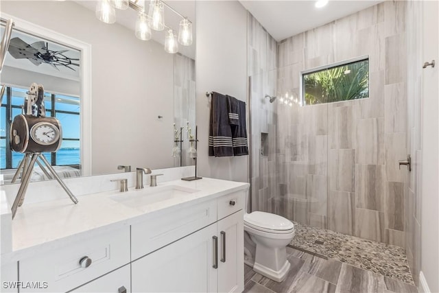 bathroom with ceiling fan, a water view, vanity, a tile shower, and toilet