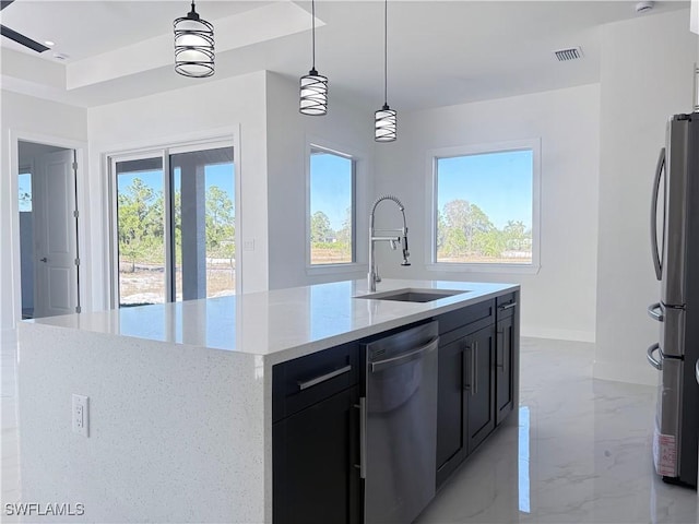 kitchen with a kitchen island with sink, sink, appliances with stainless steel finishes, decorative light fixtures, and light stone counters