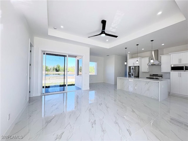 kitchen featuring wall chimney exhaust hood, white cabinetry, appliances with stainless steel finishes, and a tray ceiling