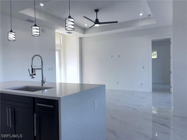 kitchen with a raised ceiling, a kitchen island with sink, sink, and decorative light fixtures