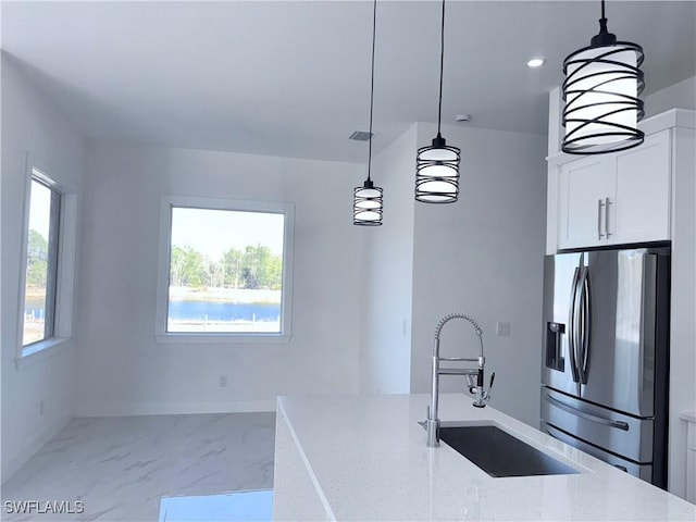 kitchen with light stone countertops, stainless steel refrigerator with ice dispenser, hanging light fixtures, and sink