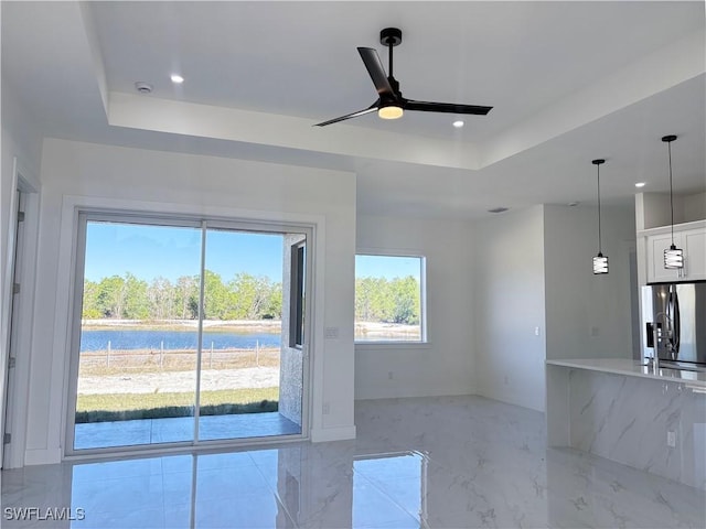 unfurnished living room with a raised ceiling, ceiling fan, and a water view