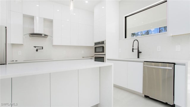 kitchen featuring sink, stainless steel appliances, wall chimney range hood, tasteful backsplash, and white cabinets