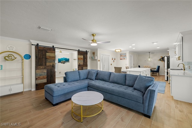 living room with a barn door, light hardwood / wood-style floors, and crown molding