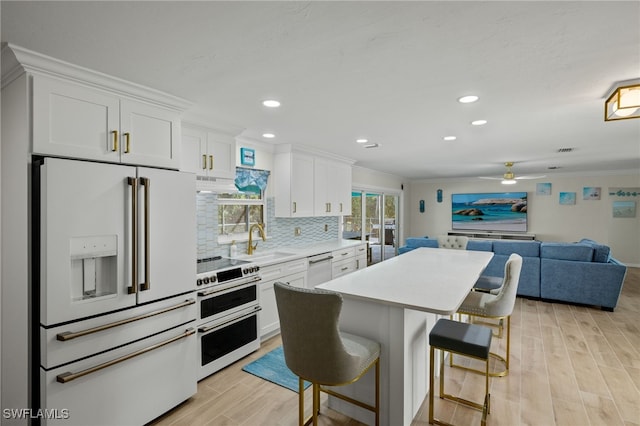 kitchen featuring white appliances, white cabinets, a kitchen breakfast bar, sink, and light hardwood / wood-style flooring