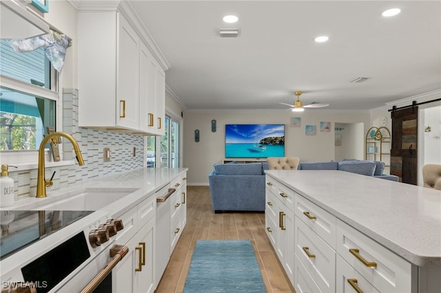 kitchen featuring white cabinetry, a barn door, light hardwood / wood-style flooring, backsplash, and ornamental molding