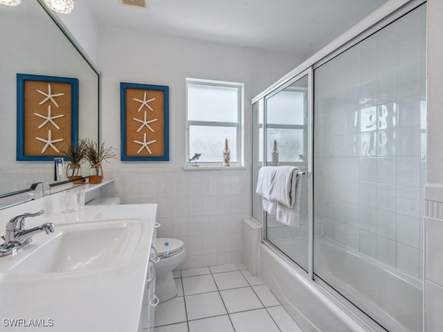 full bathroom featuring tile patterned floors, combined bath / shower with glass door, sink, toilet, and tile walls