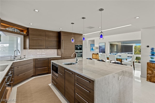 kitchen featuring sink, a center island with sink, pendant lighting, and stainless steel microwave