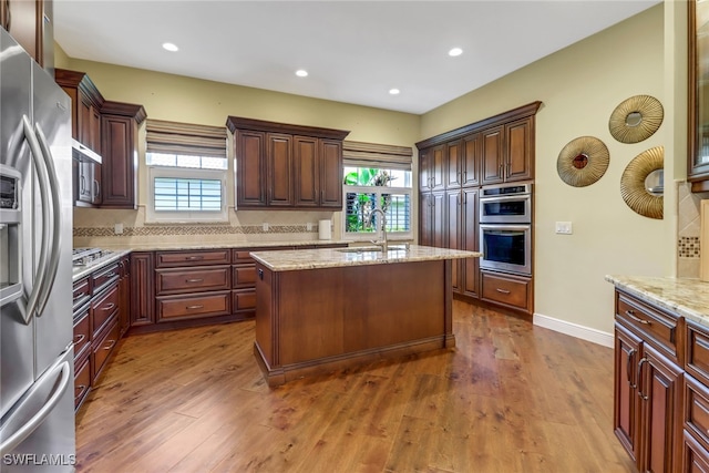 kitchen featuring dark wood finished floors, a center island, light stone countertops, stainless steel appliances, and a sink