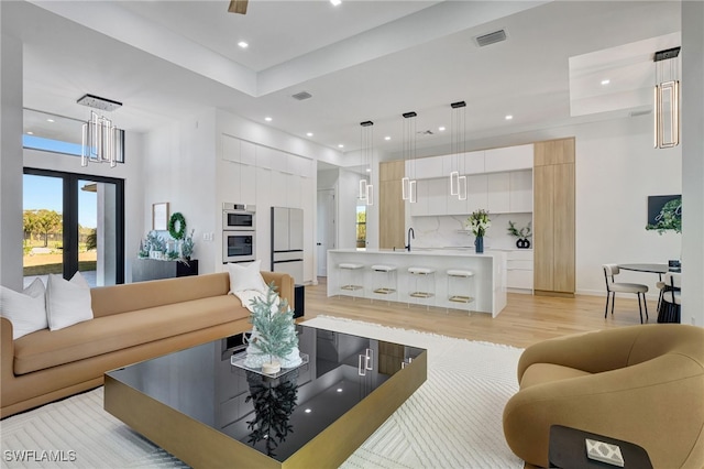 living room featuring a high ceiling, sink, and light hardwood / wood-style floors