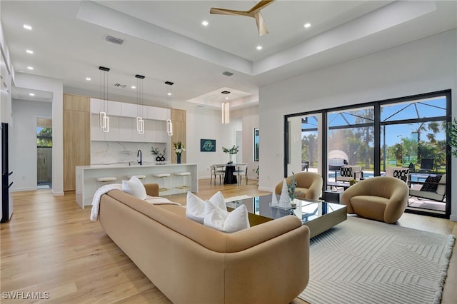 living room featuring a tray ceiling, a healthy amount of sunlight, and light wood-type flooring