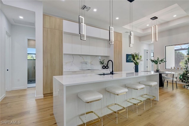 kitchen featuring sink, decorative light fixtures, white cabinets, and a center island with sink