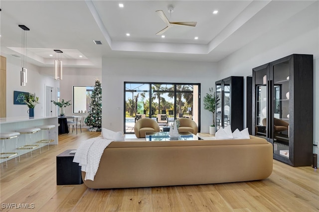 living room with ceiling fan, a raised ceiling, light wood-type flooring, and a towering ceiling