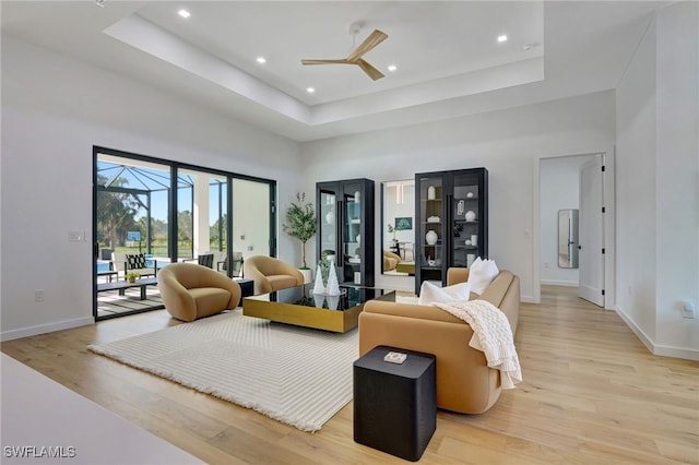 living room with ceiling fan, a raised ceiling, a high ceiling, and light wood-type flooring