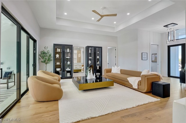 living room with ceiling fan, a towering ceiling, a raised ceiling, and light wood-type flooring