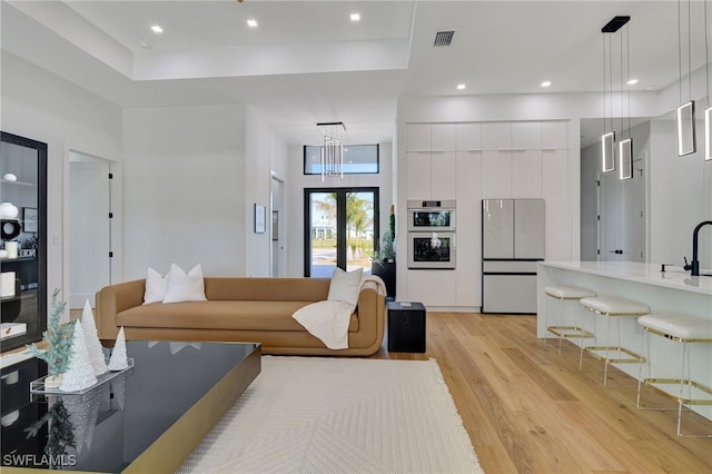 living room featuring a tray ceiling, light hardwood / wood-style floors, french doors, and a towering ceiling