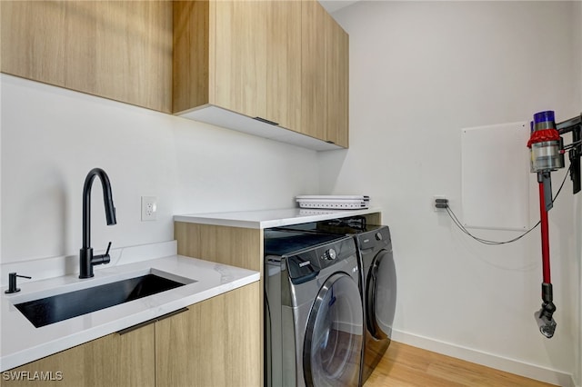 clothes washing area featuring sink, cabinets, washing machine and clothes dryer, and light wood-type flooring