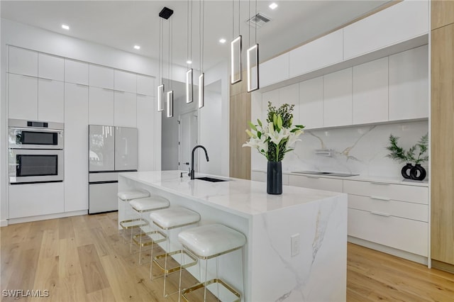 kitchen with sink, a kitchen island with sink, white cabinetry, white refrigerator, and decorative light fixtures