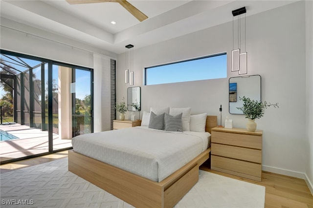 bedroom with multiple windows, a tray ceiling, access to outside, and light hardwood / wood-style flooring