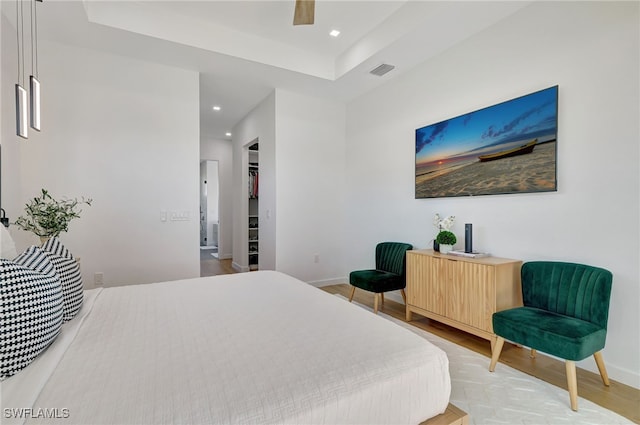 bedroom featuring a walk in closet, wood-type flooring, a tray ceiling, a closet, and ceiling fan