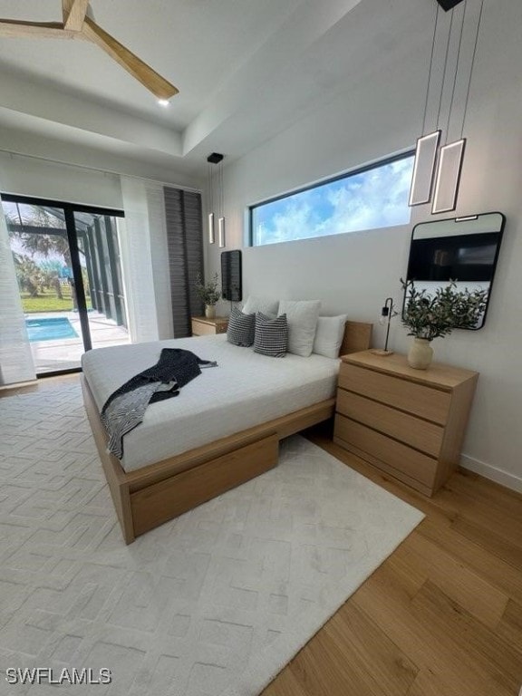 bedroom featuring access to exterior, a tray ceiling, and light hardwood / wood-style flooring