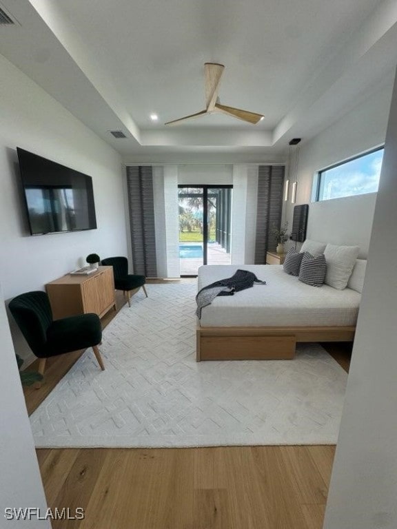 bedroom with a raised ceiling, hardwood / wood-style floors, access to exterior, and ceiling fan