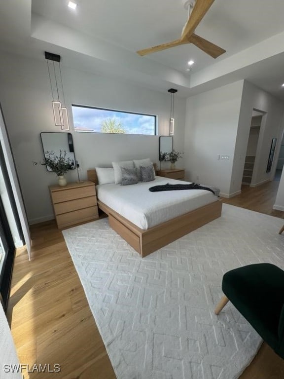 bedroom featuring ceiling fan, a raised ceiling, and light wood-type flooring