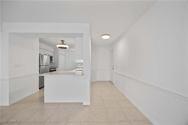 kitchen featuring kitchen peninsula, white cabinetry, light tile patterned floors, and appliances with stainless steel finishes