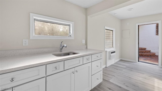 kitchen with white cabinets, light wood-type flooring, sink, and a wall unit AC