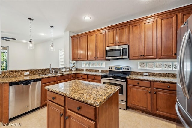 kitchen with sink, ceiling fan, appliances with stainless steel finishes, a kitchen island, and light stone counters