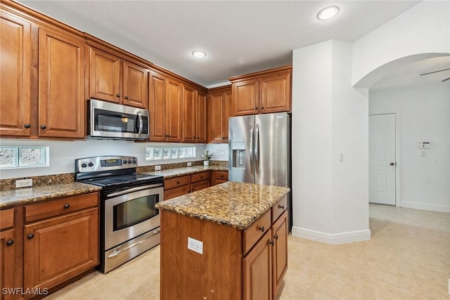 kitchen featuring ceiling fan, a center island, stainless steel appliances, and stone counters