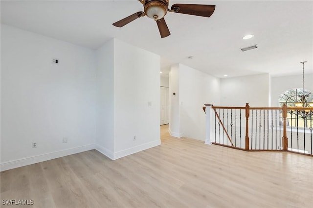 empty room featuring ceiling fan with notable chandelier and light hardwood / wood-style floors