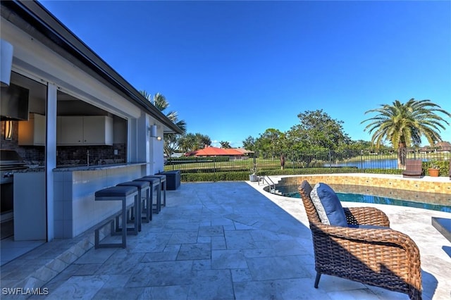 view of patio featuring a bar, a water view, and a fenced in pool