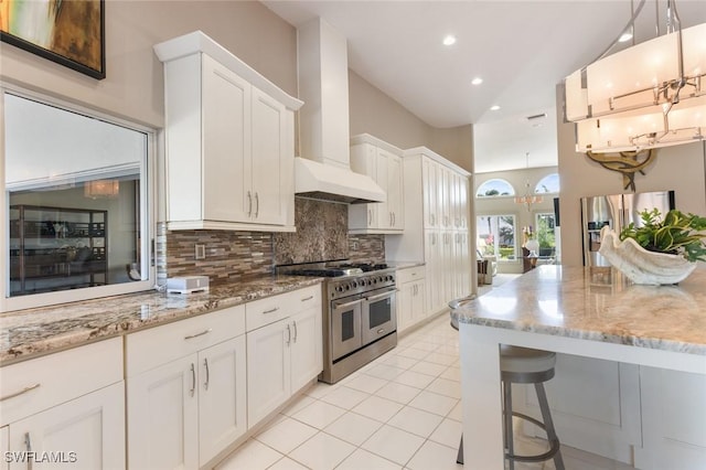 kitchen with white cabinets, hanging light fixtures, appliances with stainless steel finishes, tasteful backsplash, and custom range hood