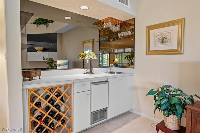 bar with white cabinetry, sink, and light carpet