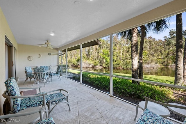 sunroom featuring ceiling fan and a water view