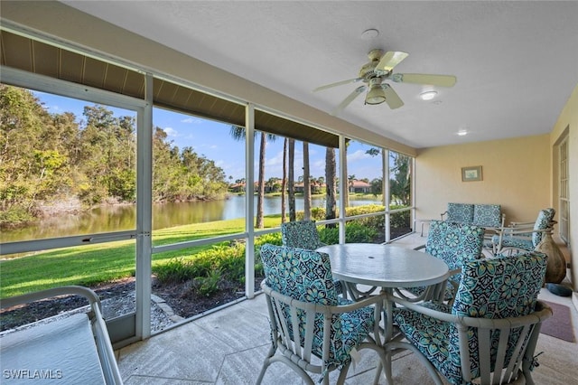 sunroom with ceiling fan and a water view