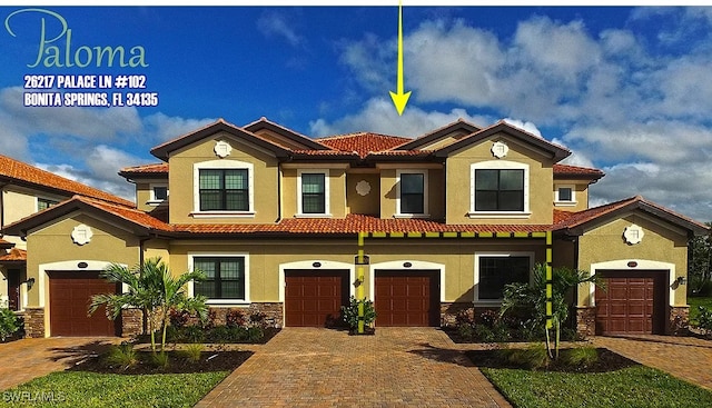 view of front of house featuring a tiled roof, driveway, stone siding, an attached garage, and stucco siding