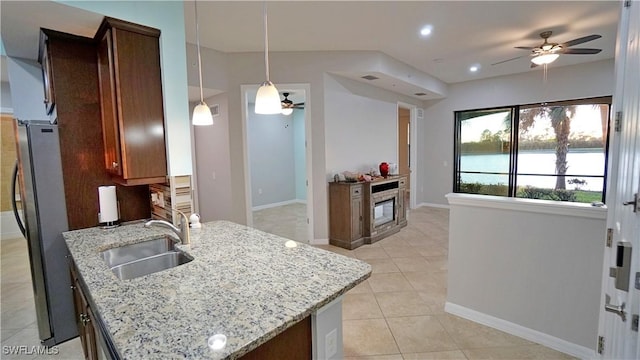 kitchen with sink, ceiling fan, stainless steel fridge, light stone countertops, and decorative light fixtures