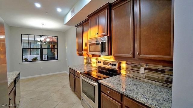 kitchen featuring appliances with stainless steel finishes, tasteful backsplash, light stone counters, light tile patterned floors, and a notable chandelier