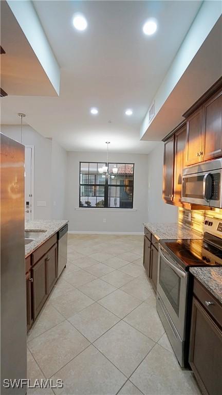 kitchen with light stone countertops, hanging light fixtures, stainless steel appliances, an inviting chandelier, and decorative backsplash