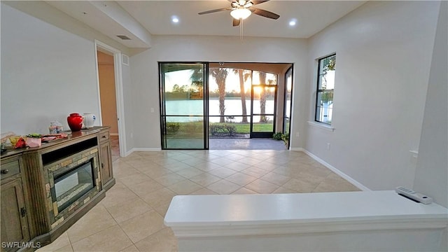 tiled living room with plenty of natural light, ceiling fan, and a stone fireplace