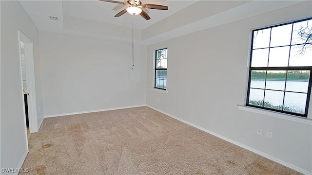 unfurnished room featuring a tray ceiling, visible vents, baseboards, carpet, and a ceiling fan