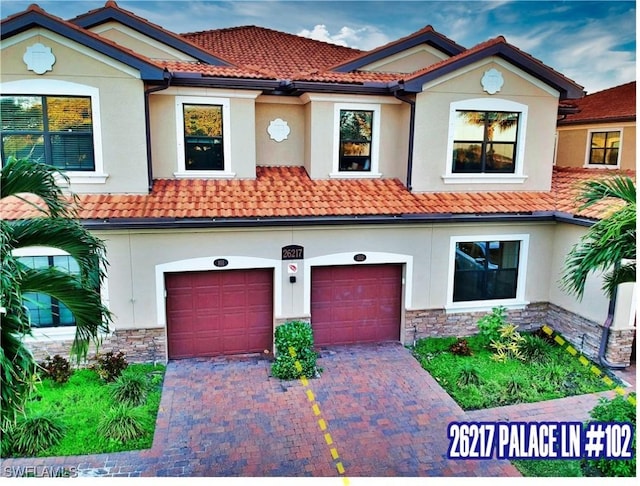 view of front of house featuring driveway, stone siding, a tiled roof, a garage, and stucco siding
