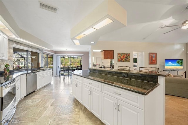 kitchen with range, stainless steel dishwasher, ceiling fan, dark stone countertops, and white cabinetry