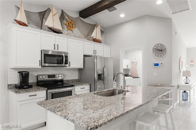 kitchen with stainless steel appliances, a kitchen island with sink, sink, beamed ceiling, and white cabinetry