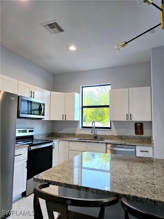 kitchen featuring visible vents, appliances with stainless steel finishes, light stone counters, white cabinetry, and a sink